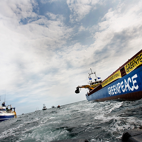 Greenpeace-fartyg på öppet hav under en aktion, med andra båtar i bakgrunden och vågigt vatten.