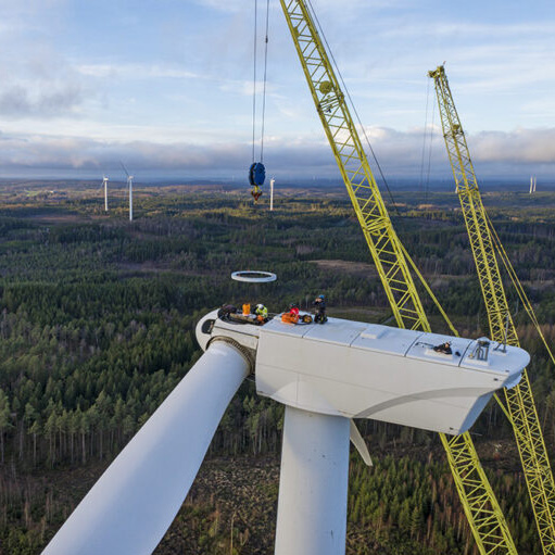 Drönarbild av ett vindkraftverk under underhåll, med tekniker och lyftkranar i arbete på hög höjd