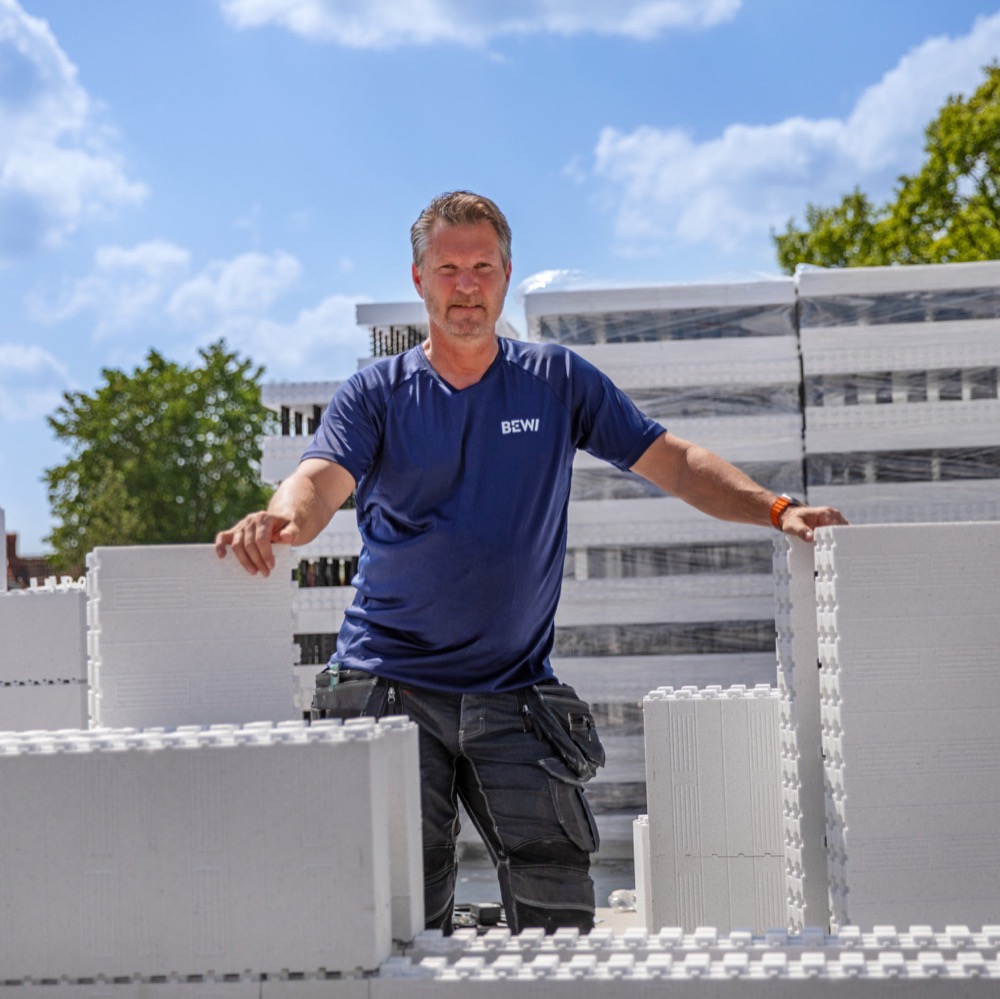 Medarbetare från BEWI arbetar utomhus med byggmaterial, fotograferad i en miljö med staplade isoleringsblock och blå himmel.
