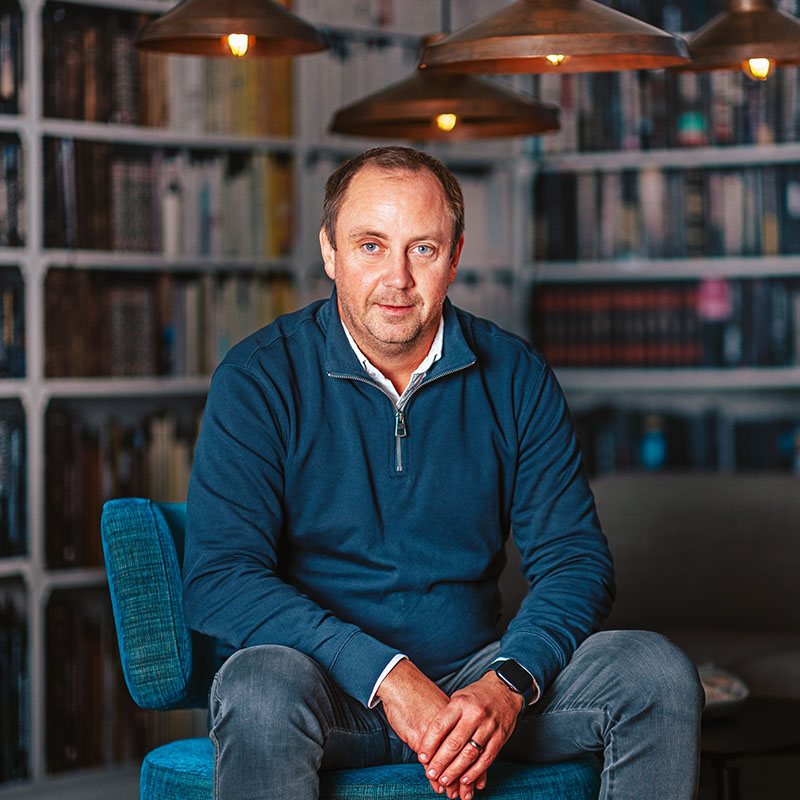 Porträtt av Daniel Ryttare från Riverty i Varberg, sittande i en modern miljö med bokhyllor i bakgrunden.