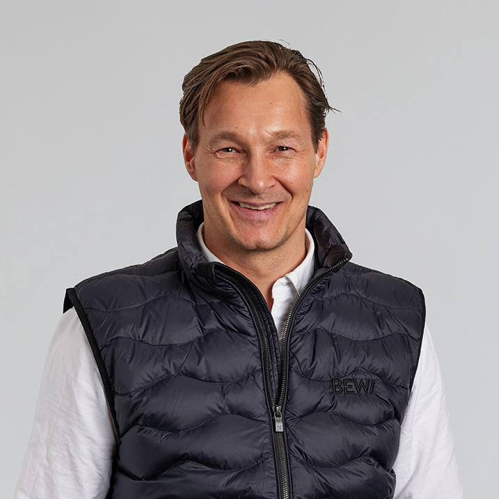 Porträtt av en man i en svart vadderad väst med BEWI-logotyp, fotograferad mot en ljus bakgrund för tjänsten personalfoto.